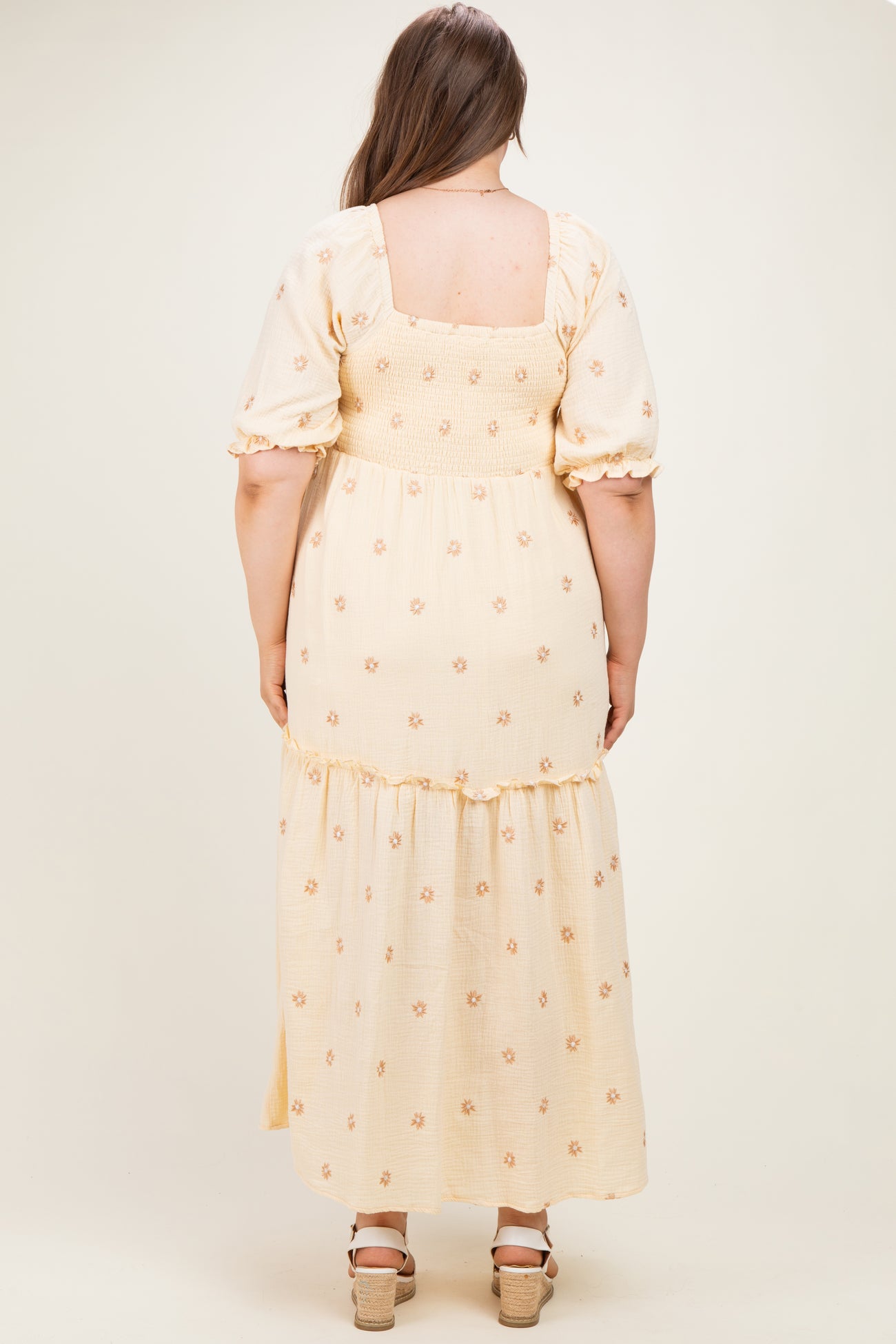 woman wearing a yellow floral maternity plus maxi dress with puff sleeves and a tiered skirt, showcasing a baby bump