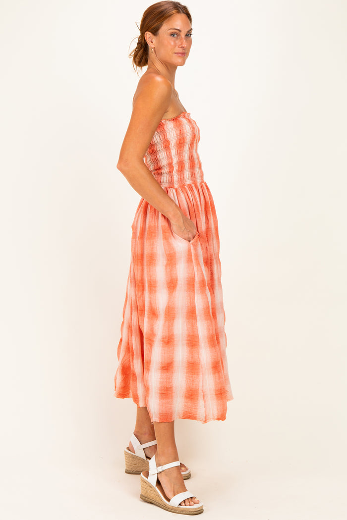 woman wearing an orange and white checkered midi dress with a smocked bodice and side pockets, styled with wedge sandals