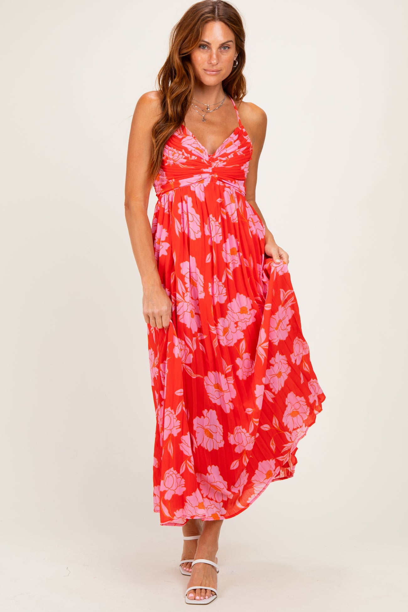 woman wearing a red maxi dress with pink floral print and a fitted bust, posing with one hand on her hip