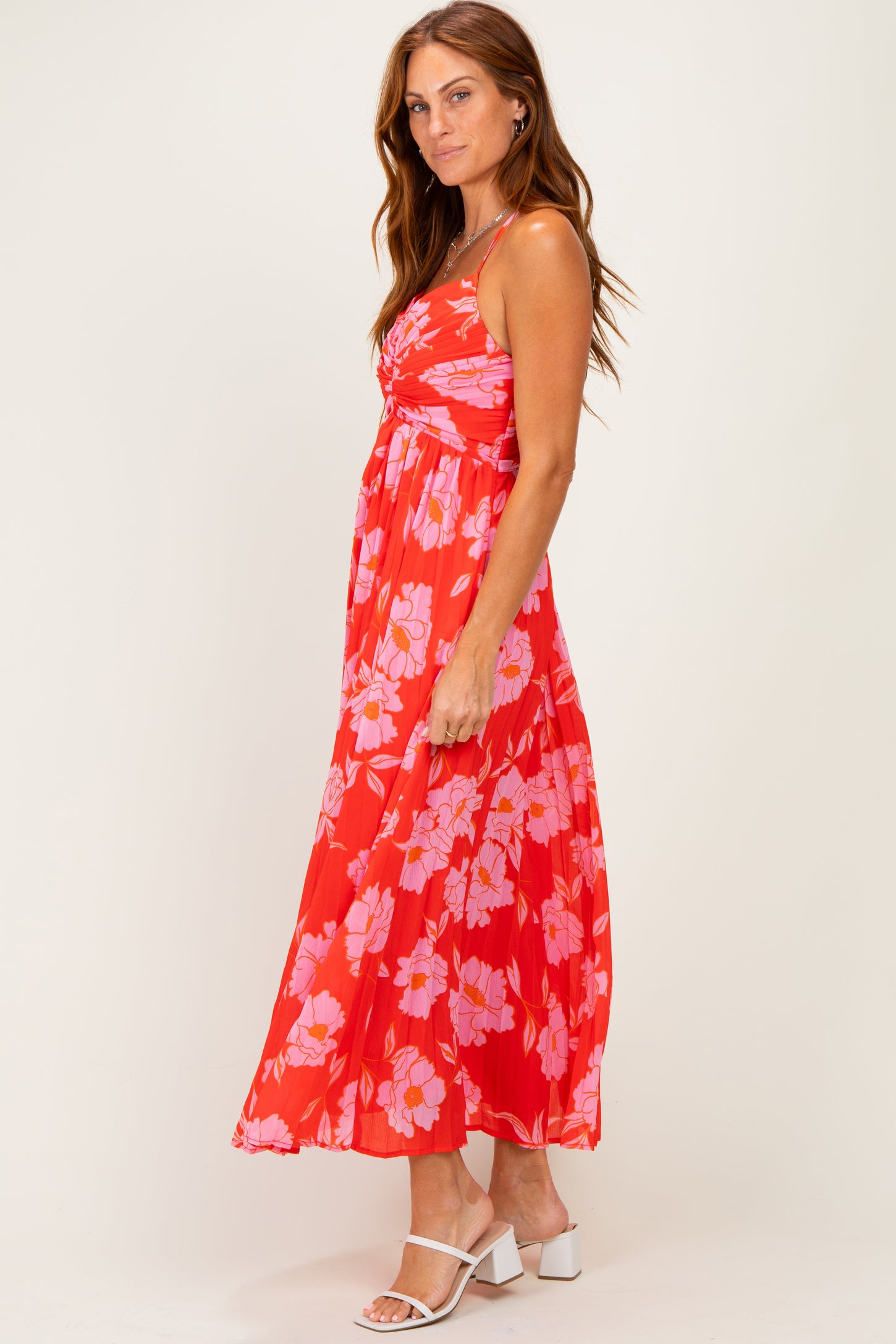 woman wearing a red floral maxi dress with a fitted bodice and flowing skirt, posing sideways with a smile