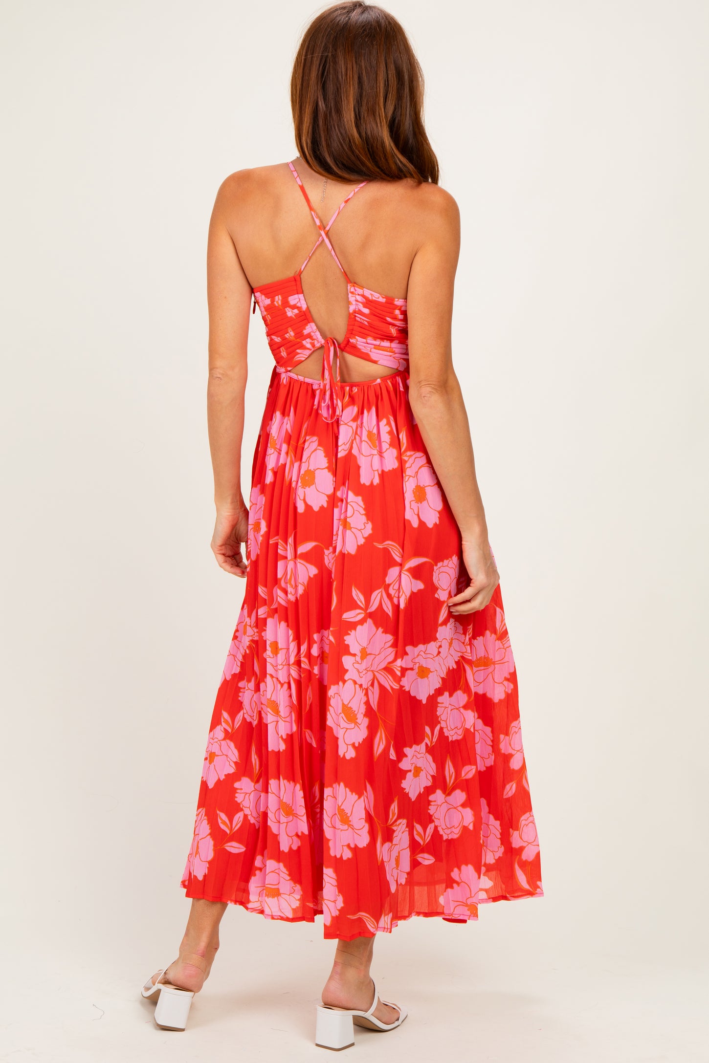 woman wearing a red floral maxi dress with a crisscross back design and pleated skirt