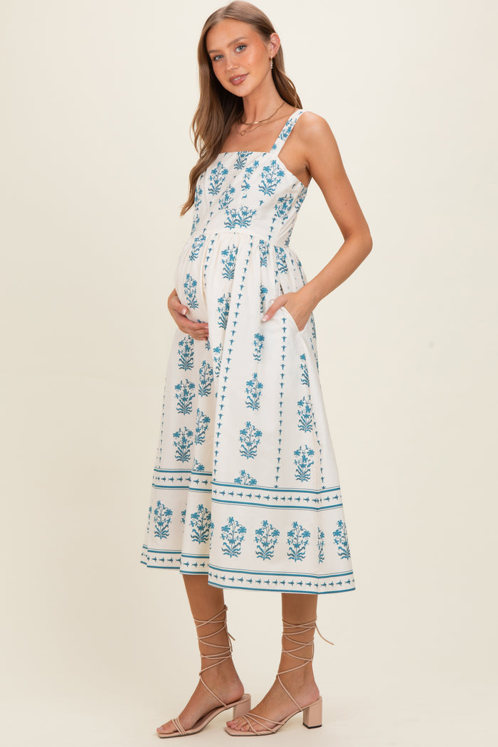 woman wearing a white maternity dress with blue floral print and pockets, showing her baby bump