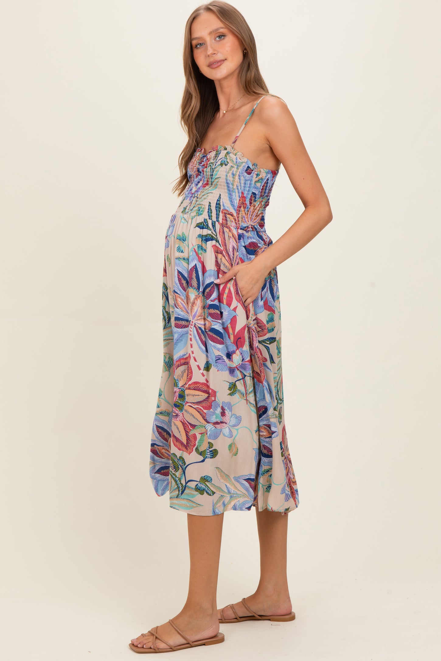 woman wearing a floral maternity dress with adjustable straps and pockets, showcasing her baby bump
