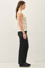 woman wearing a cream and rust striped sleeveless top and dark flared jeans, standing sideways against a plain background