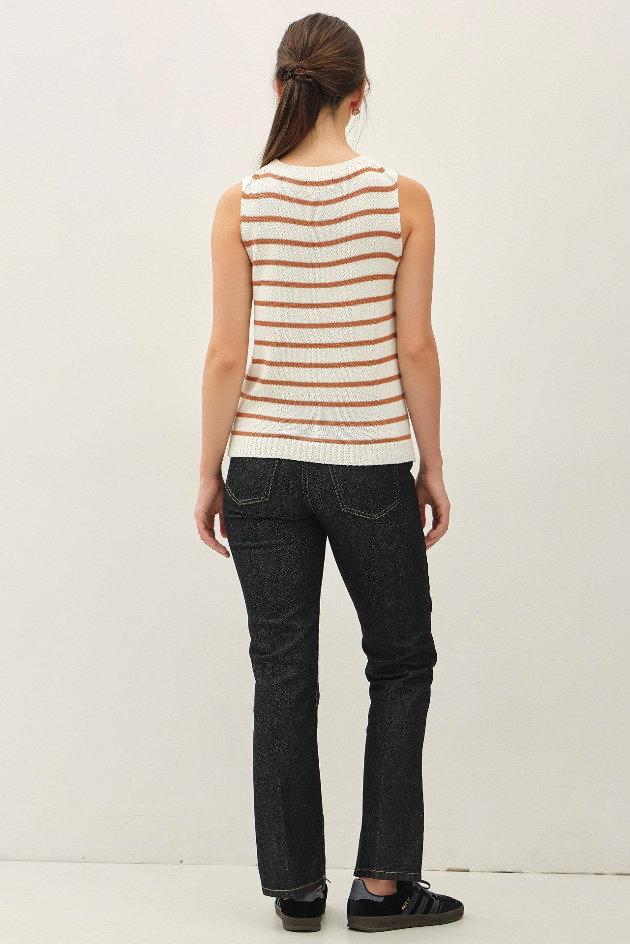 woman wearing a white and orange striped sleeveless top and black jeans, viewed from the back