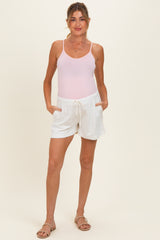 woman wearing a light pink maternity tank top and white maternity shorts with pockets.