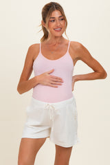 woman wearing a pink maternity tank top and white maternity shorts, holding her baby bump
