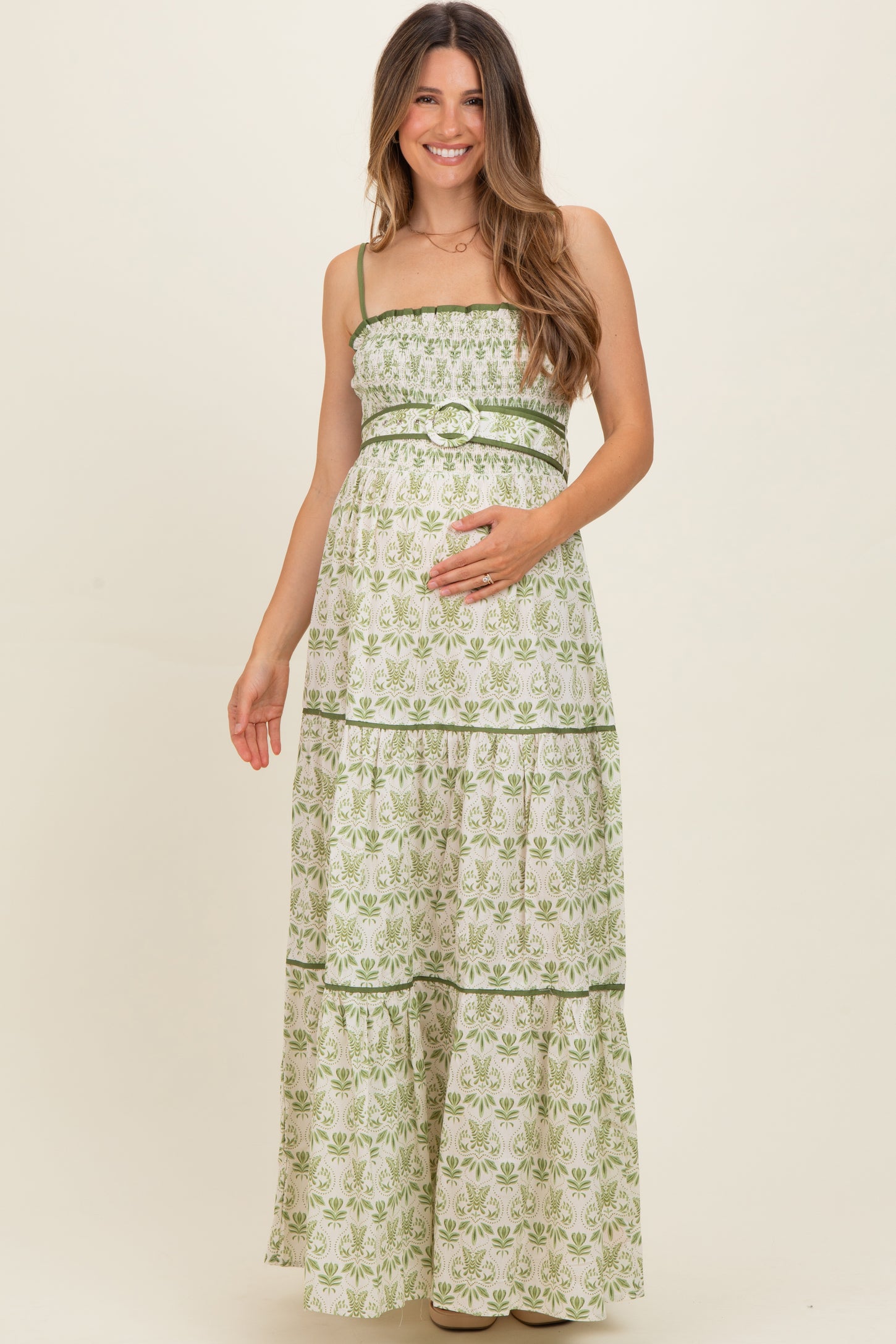 woman wearing a green and white floral print maternity maxi dress with a cinched waist and tiered skirt, holding her baby bump
