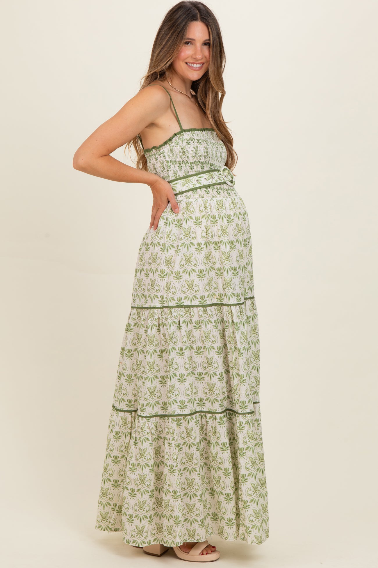 woman wearing a green and white floral print maternity maxi dress with tiered layers and a baby bump visible