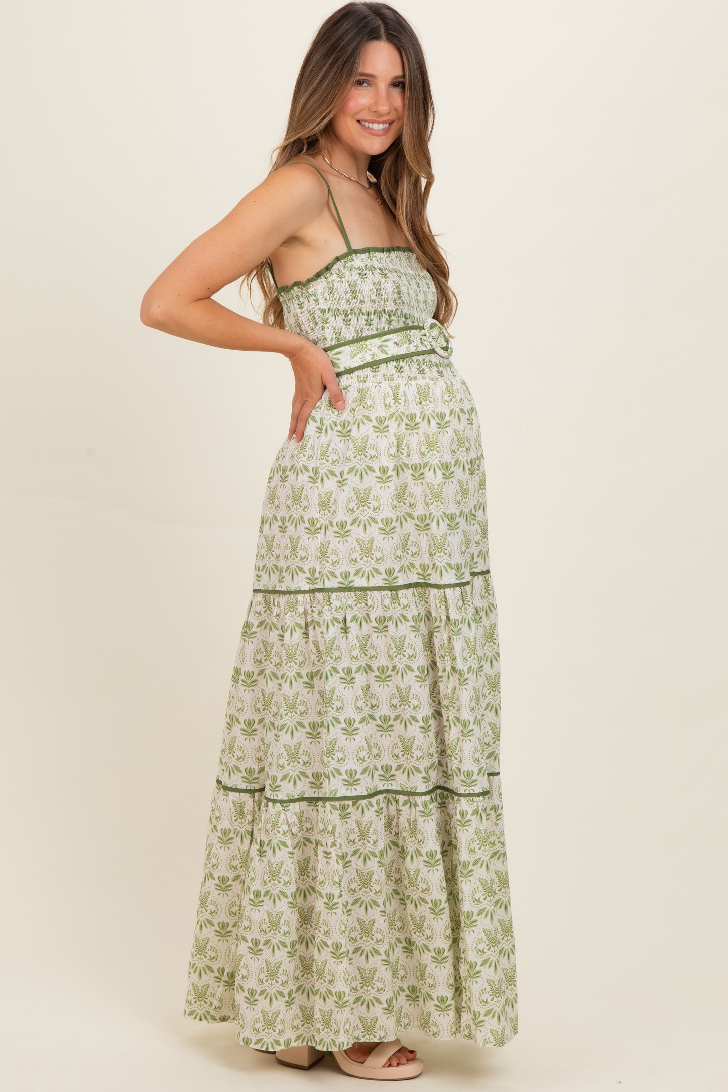 woman wearing a green and white floral print maternity maxi dress with tiered layers and a baby bump visible