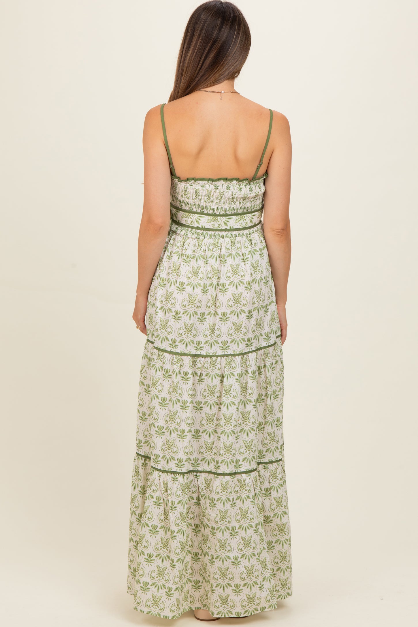 woman wearing a green and white floral maternity maxi dress with a tiered design and spaghetti straps