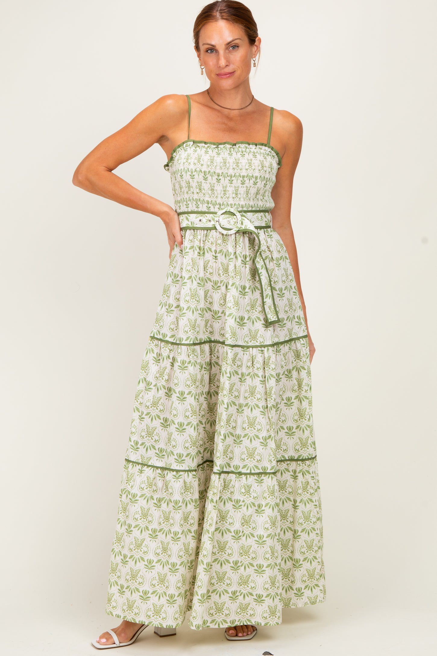 woman wearing a green and white floral maxi dress with smocked bodice and tiered skirt, posing with one hand on her hip