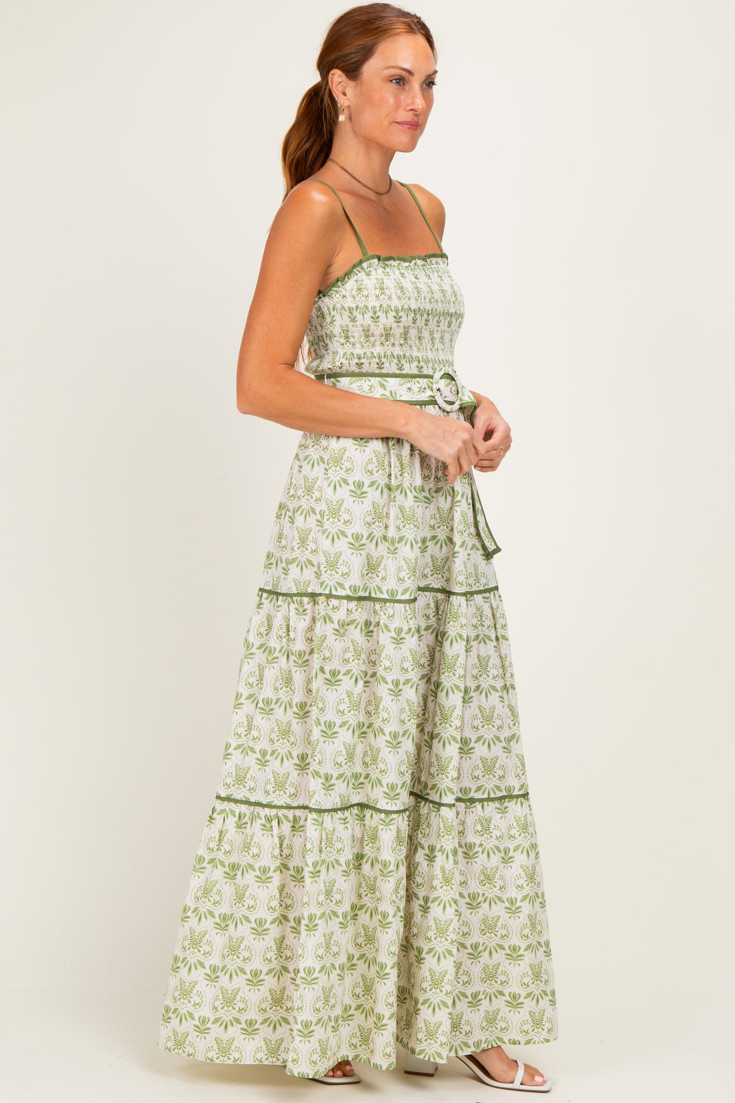 woman wearing a green and white floral maxi dress with spaghetti straps and a fitted bodice, standing in profile