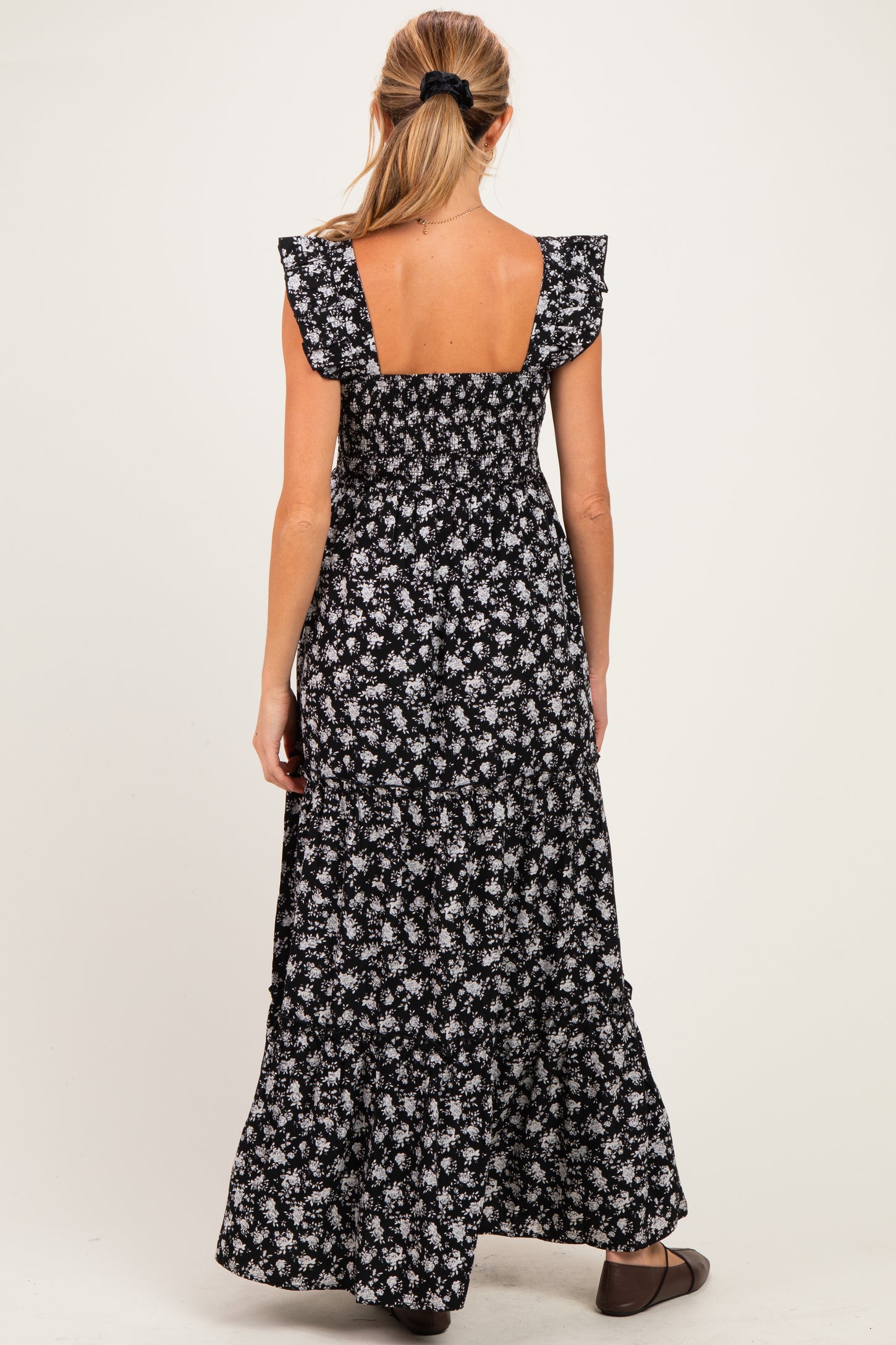 woman wearing a black floral maternity maxi dress with ruffled sleeves, showing the back view and relaxed fit