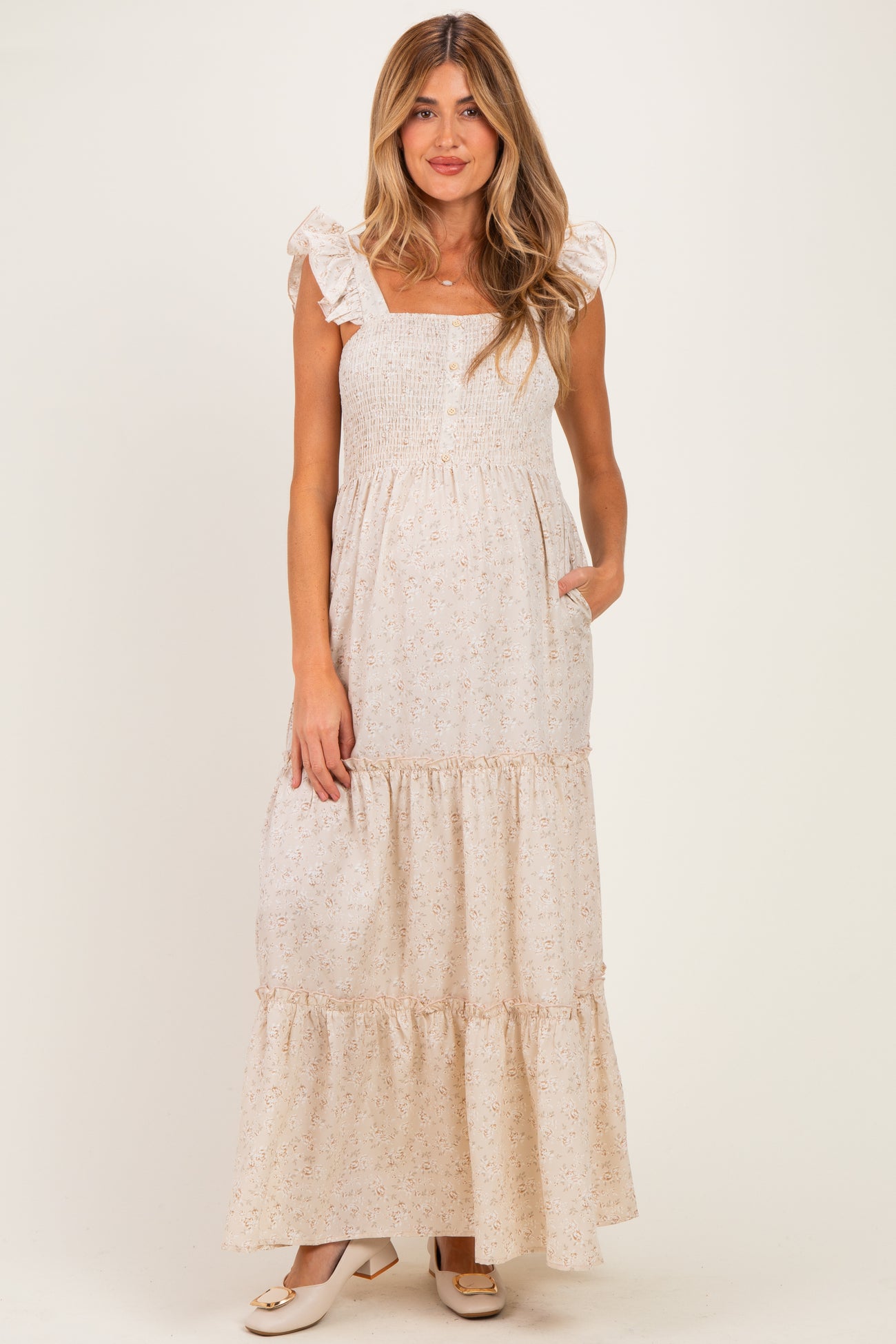 woman wearing a cream floral maternity maxi dress with ruffled straps and pockets, showing her baby bump