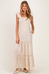 woman wearing a cream floral maternity maxi dress with ruffled straps and pockets, showing her baby bump