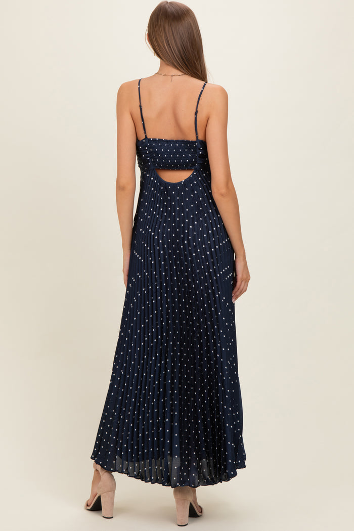 woman wearing a navy blue polka dot maternity maxi dress with a pleated skirt and cutout back detail