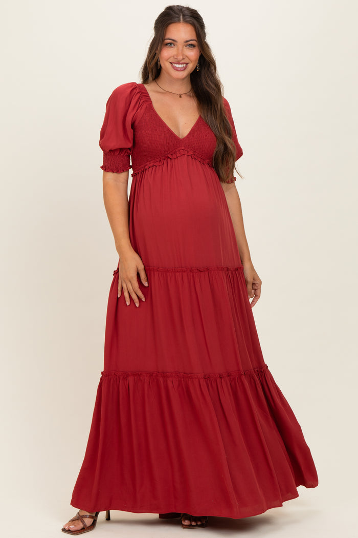 woman wearing a burgundy maternity maxi dress with puff sleeves and ruffled tiered skirt, showing her baby bump