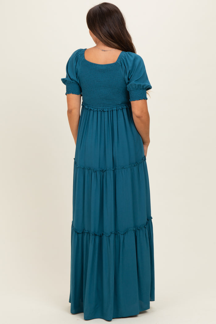 woman wearing a teal smocked maternity maxi dress with short puff sleeves and tiered design, showing a baby bump