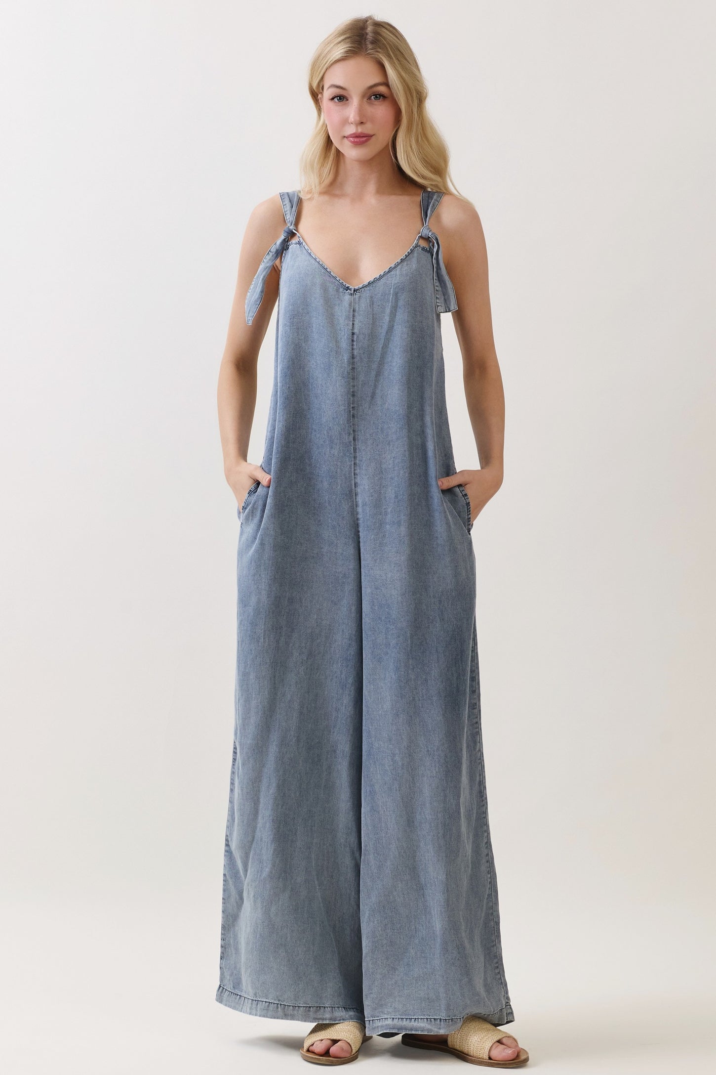 woman wearing a light blue denim jumpsuit with tie straps and side pockets