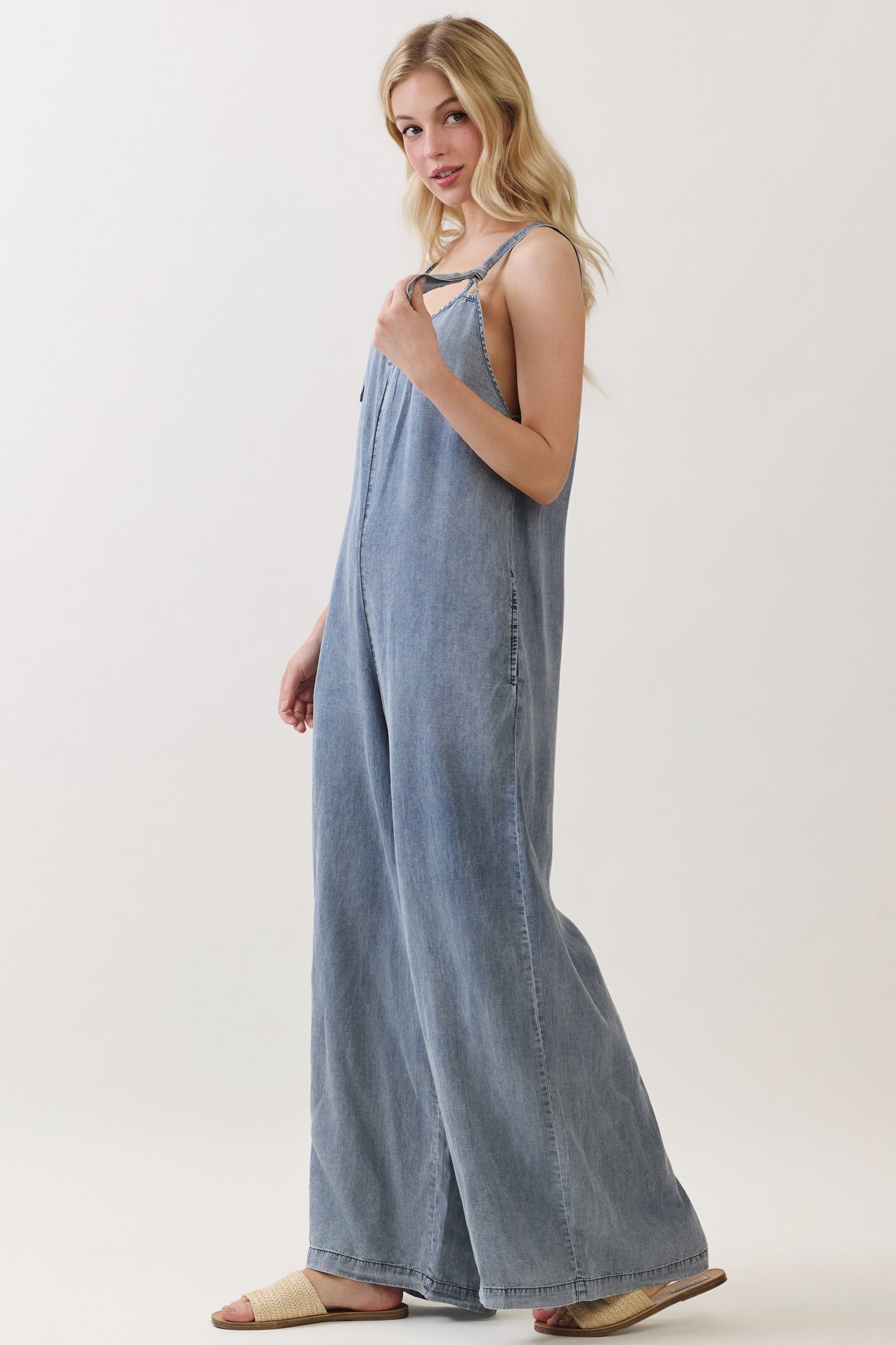 woman wearing a light blue denim jumpsuit with a relaxed fit and wide legs, styled with strappy sandals