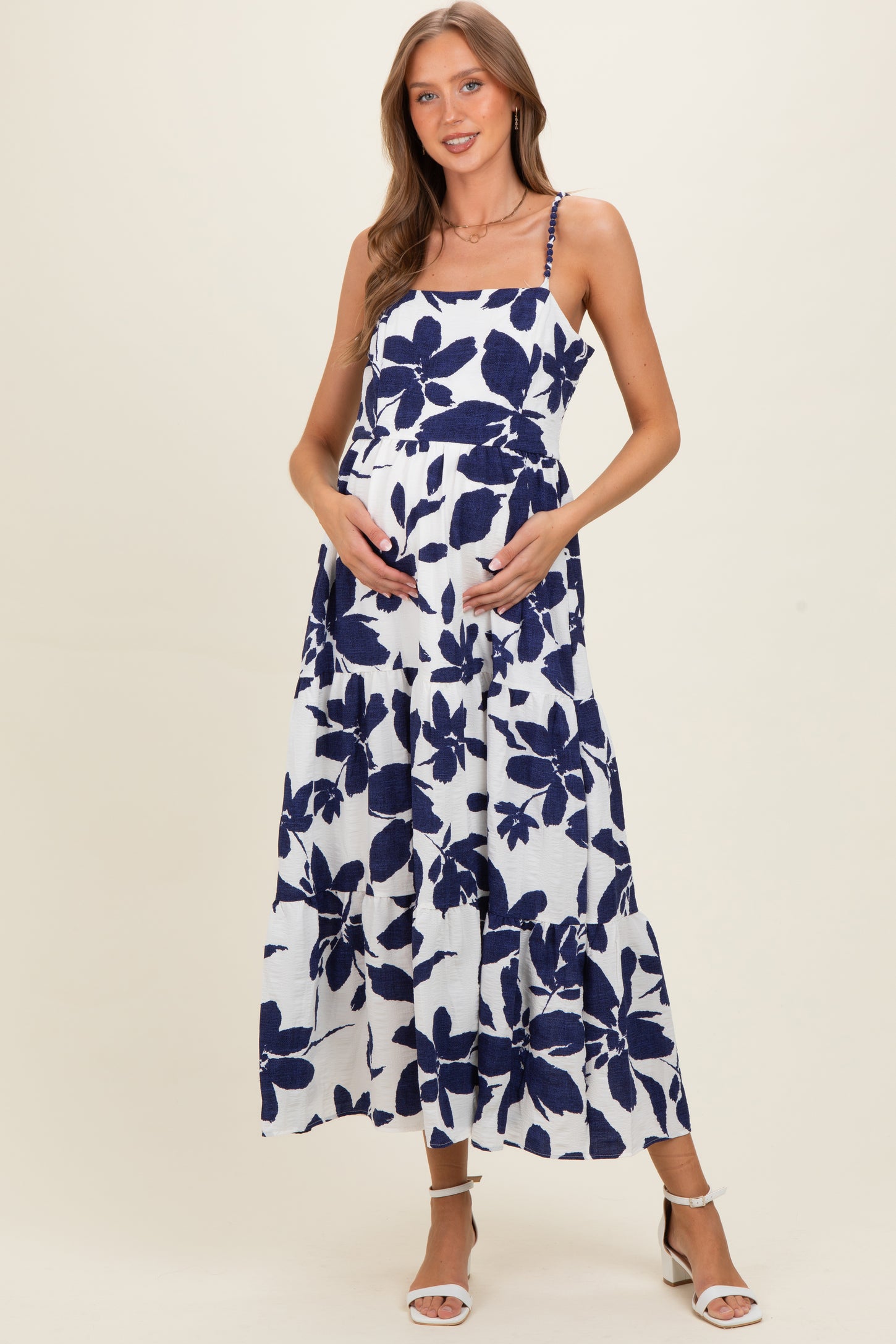 woman wearing a blue and white floral maternity maxi dress and gently cradling her baby bump