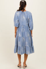 woman wearing a blue floral print midi dress with puff sleeves and a tiered skirt viewed from the back