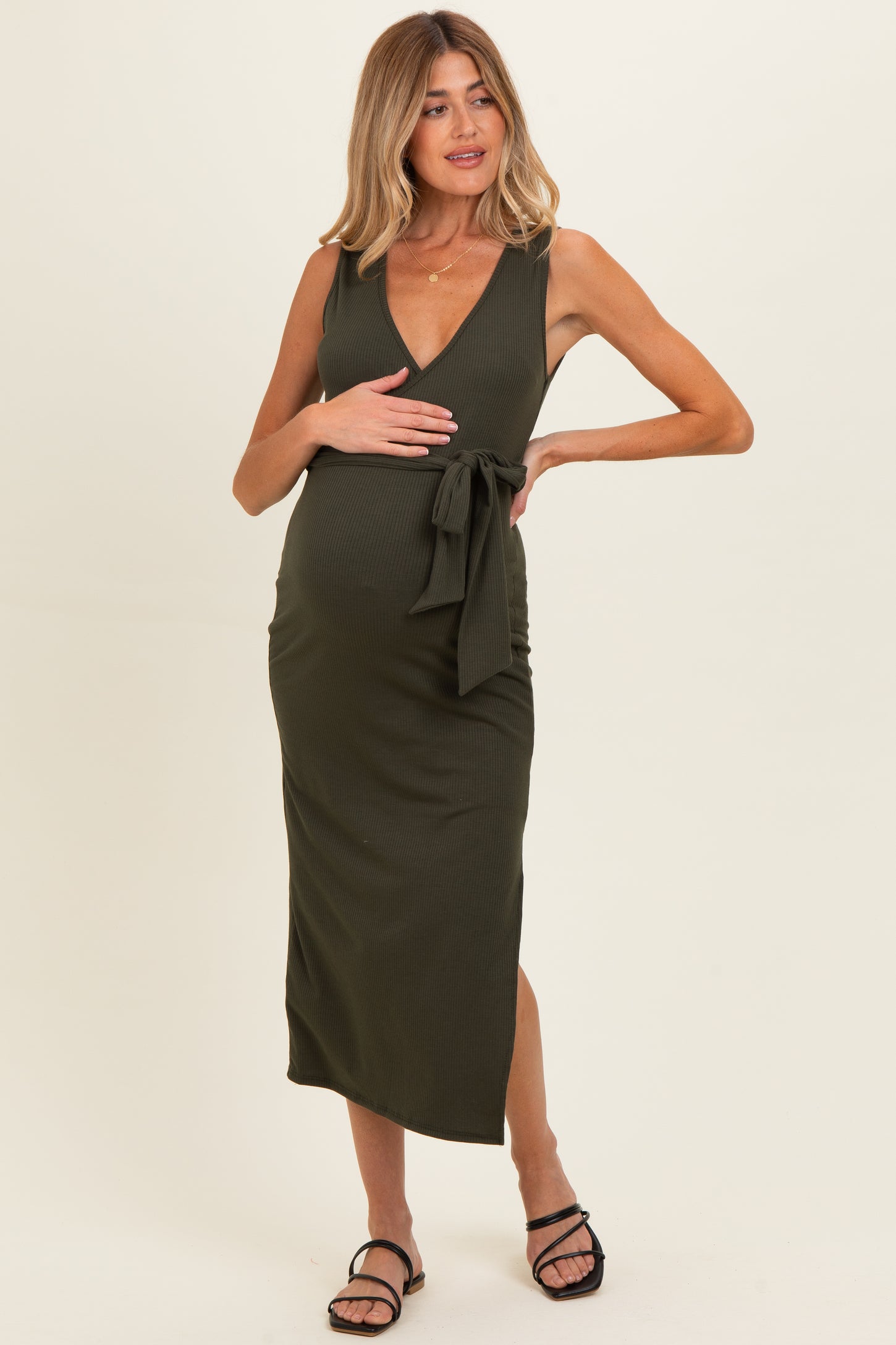 woman wearing a dark olive green maternity dress with a v-neck and a tie at the waist, showing a baby bump