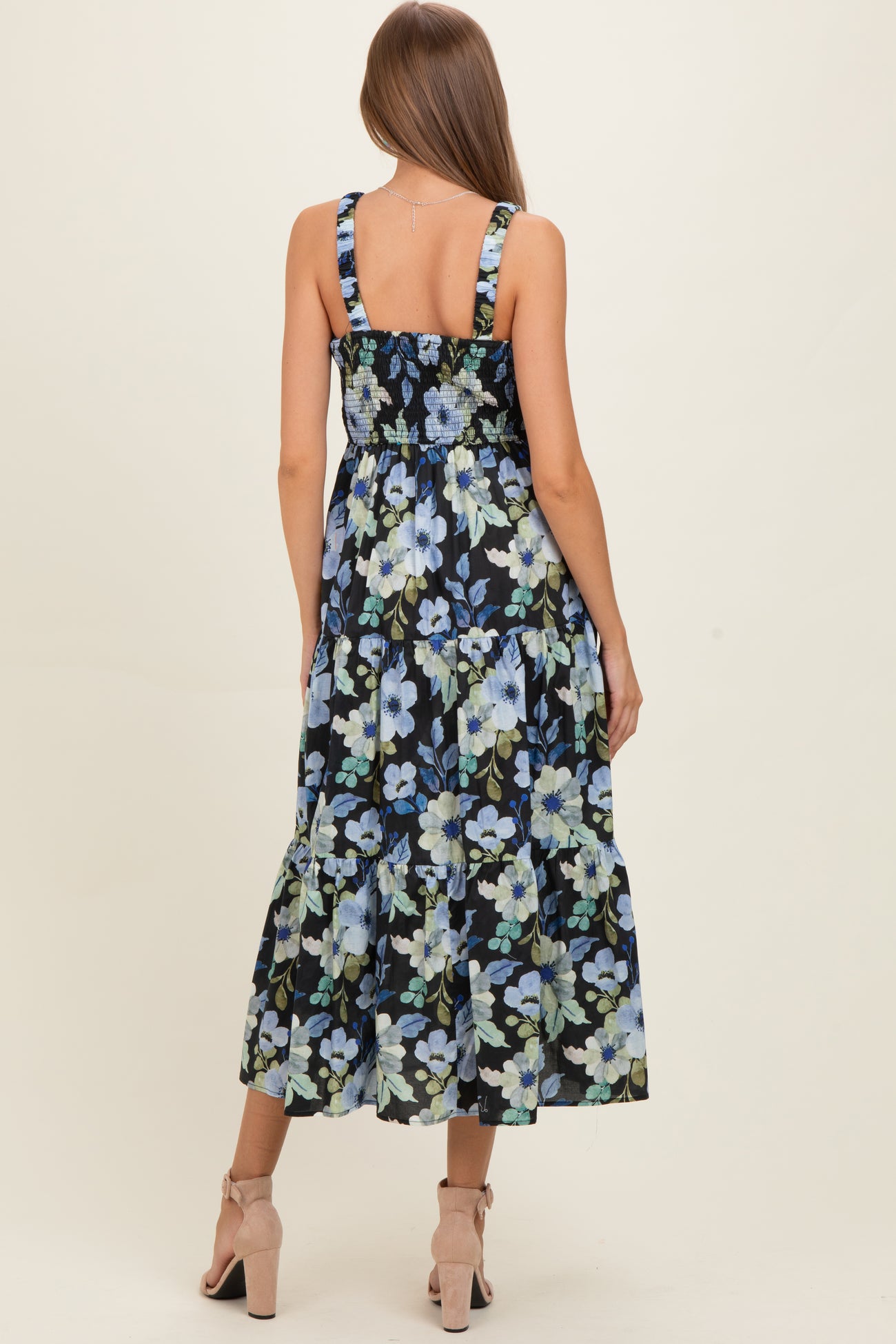 woman wearing a black floral maternity dress with smocked bodice and tiered skirt, showing the back view