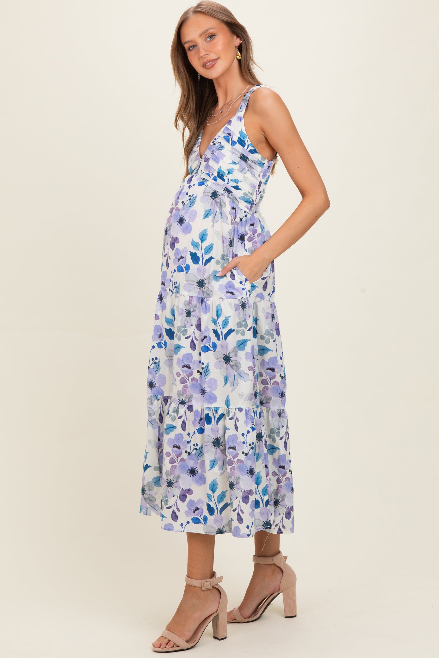 woman wearing a floral print maternity dress with pockets and a baby bump visible, styled with strappy heels