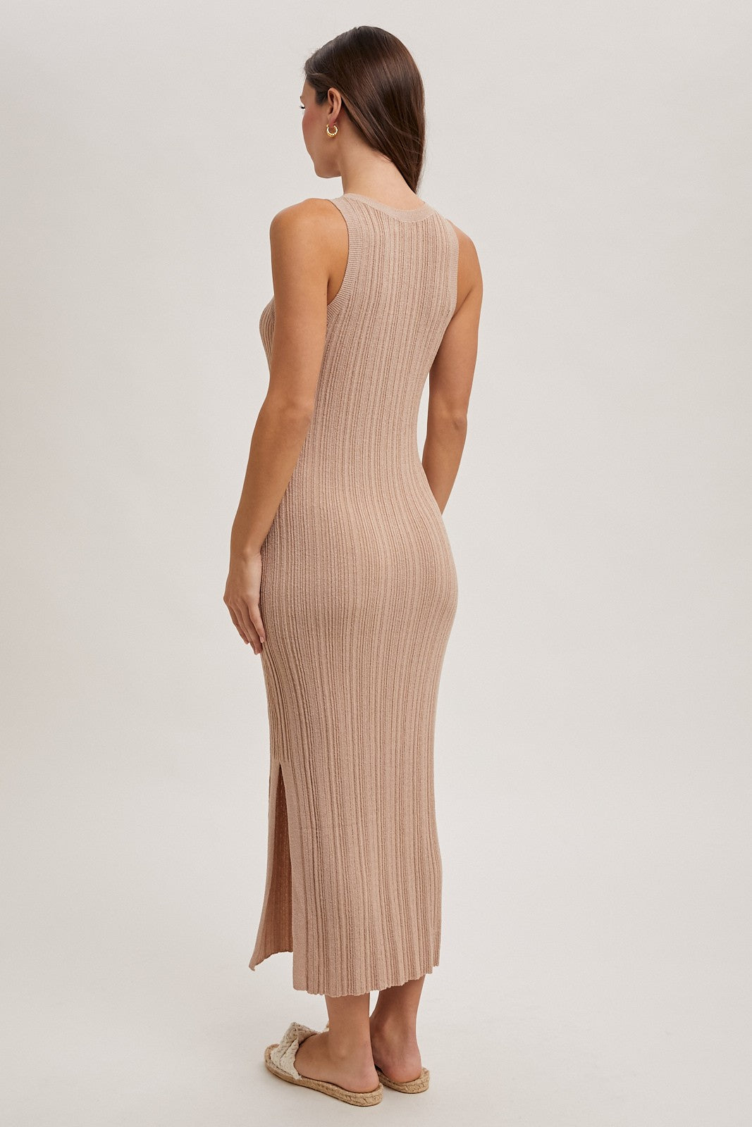woman wearing a beige ribbed knit maxi dress with a side slit, seen from the back