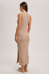 woman wearing a beige ribbed knit maxi dress with a side slit, seen from the back