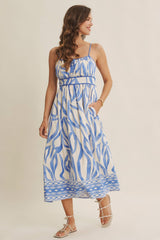 woman wearing a blue and white floral print maxi dress with spaghetti straps and pockets, smiling against a light background