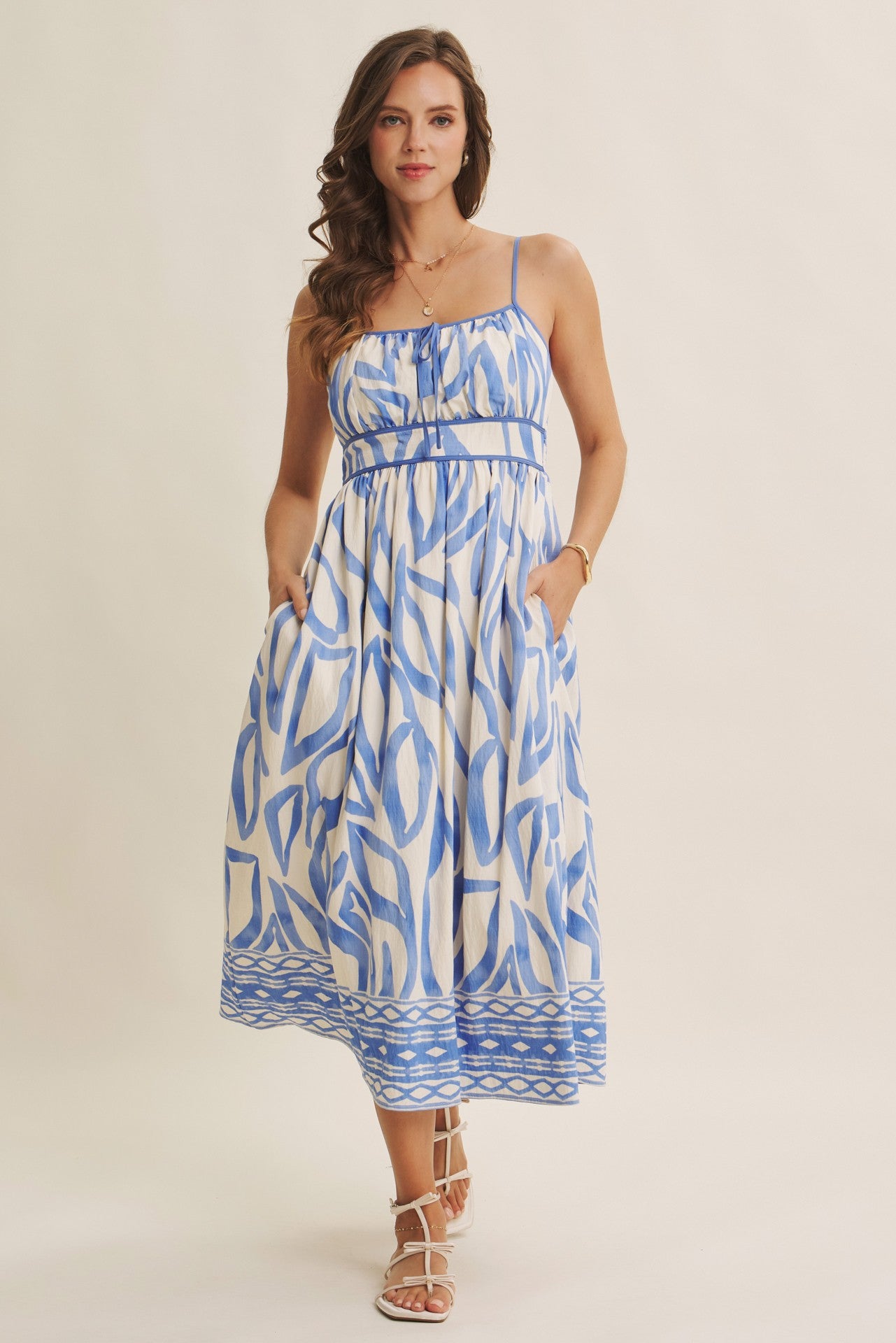 woman wearing a blue and white patterned midi dress with spaghetti straps and pockets, styled with strappy sandals