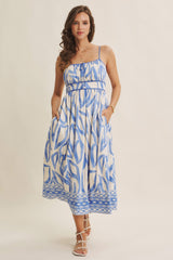woman wearing a blue and white patterned midi dress with spaghetti straps and pockets, styled with strappy sandals