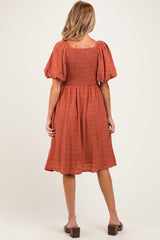 woman wearing a rust-colored maternity dress with puff sleeves and a smocked back, view from the back