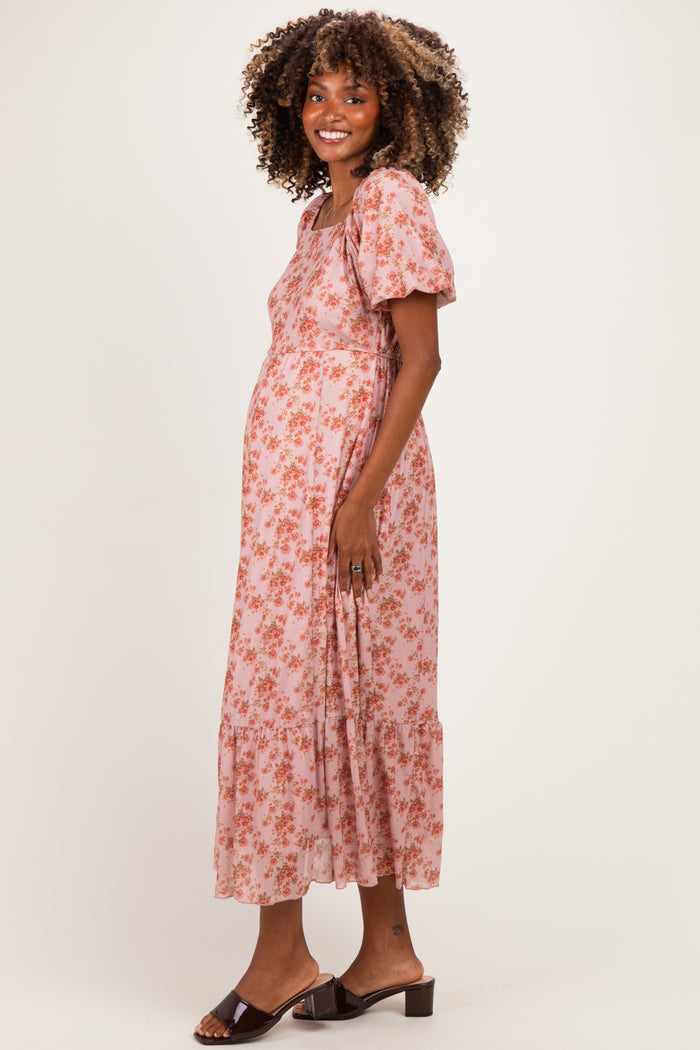 woman wearing a pink floral maternity dress with puff sleeves and a tiered skirt, showing her baby bump