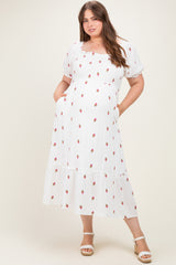 woman wearing a white maternity plus dress with red floral print and puff sleeves, showing her baby bump and pockets