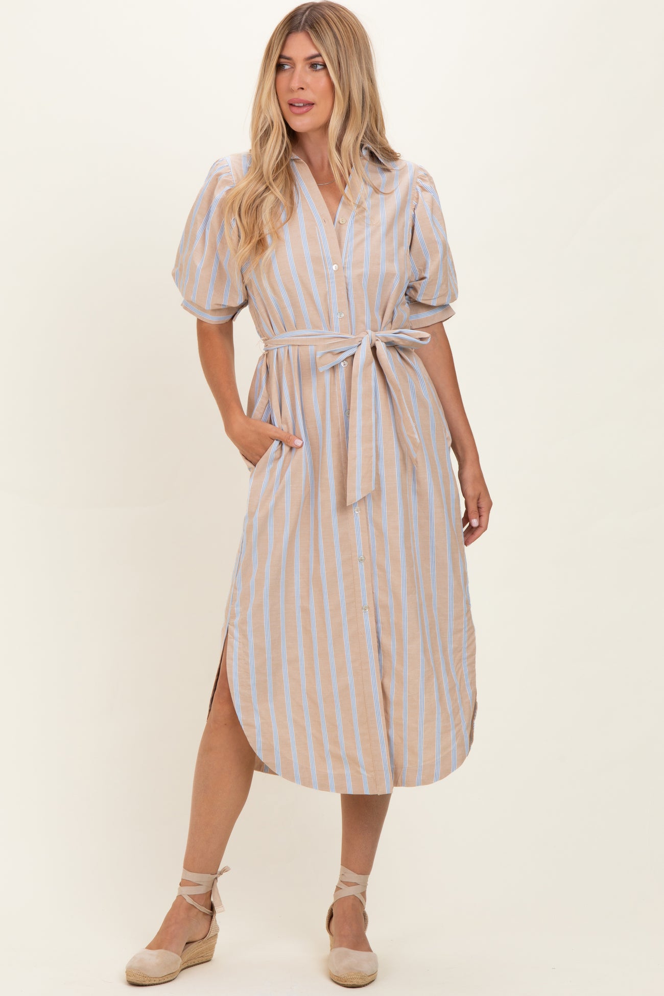 woman wearing a beige striped midi dress with puff sleeves, a tied waist, and side pockets
