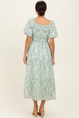 woman wearing a green and white floral midi dress with short puff sleeves and a smocked bodice, view from the back