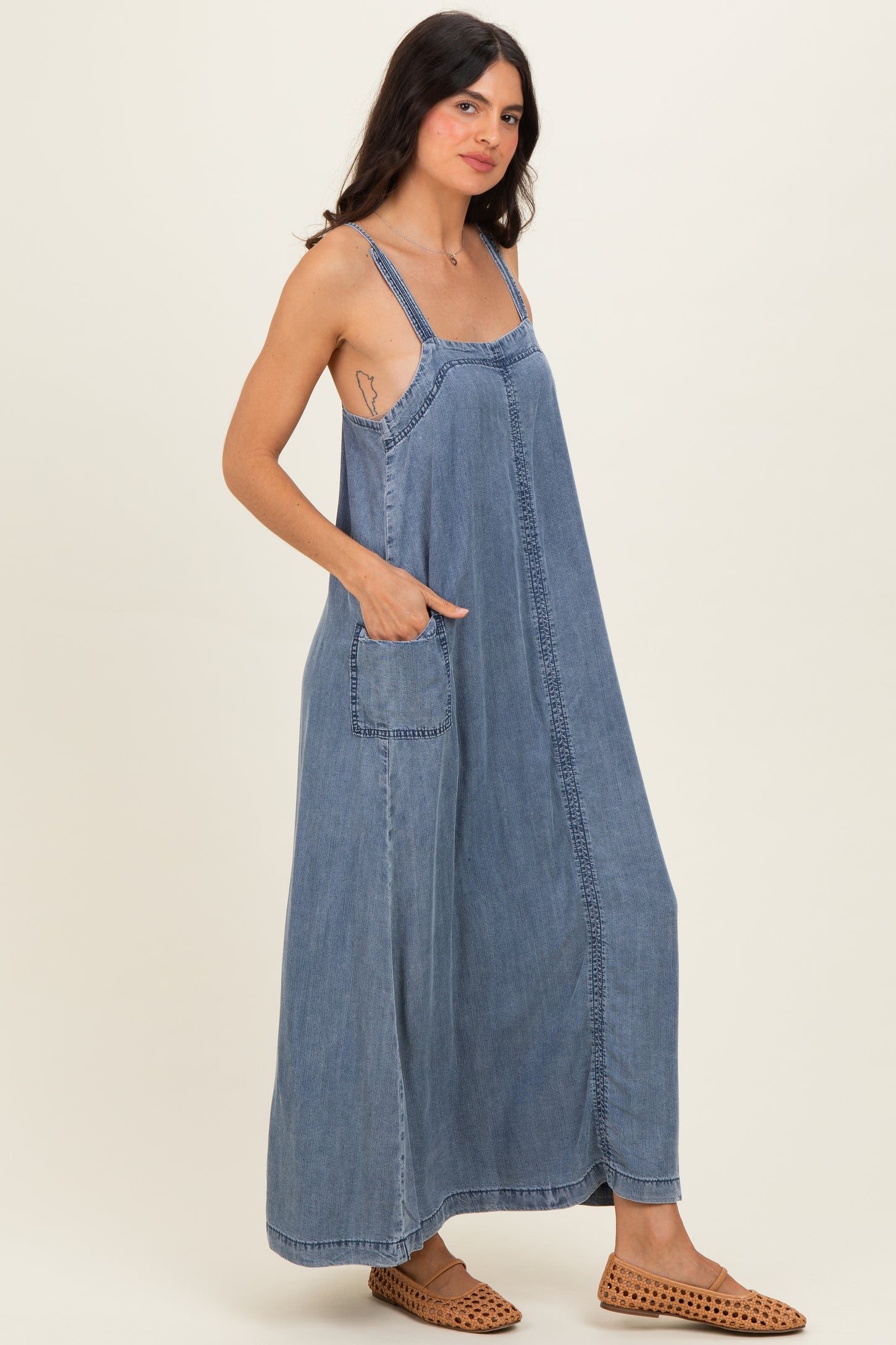 woman wearing a blue denim maxi dress with adjustable straps and side pockets