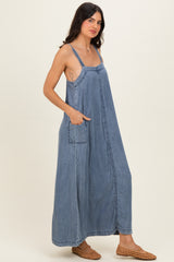 woman wearing a blue denim maxi dress with adjustable straps and side pockets