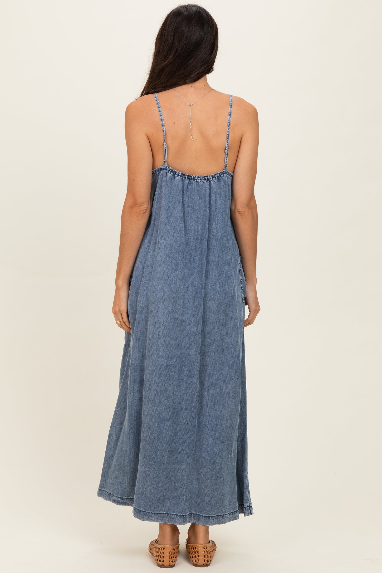 woman wearing a backless denim maxi dress with thin straps and a flowing silhouette