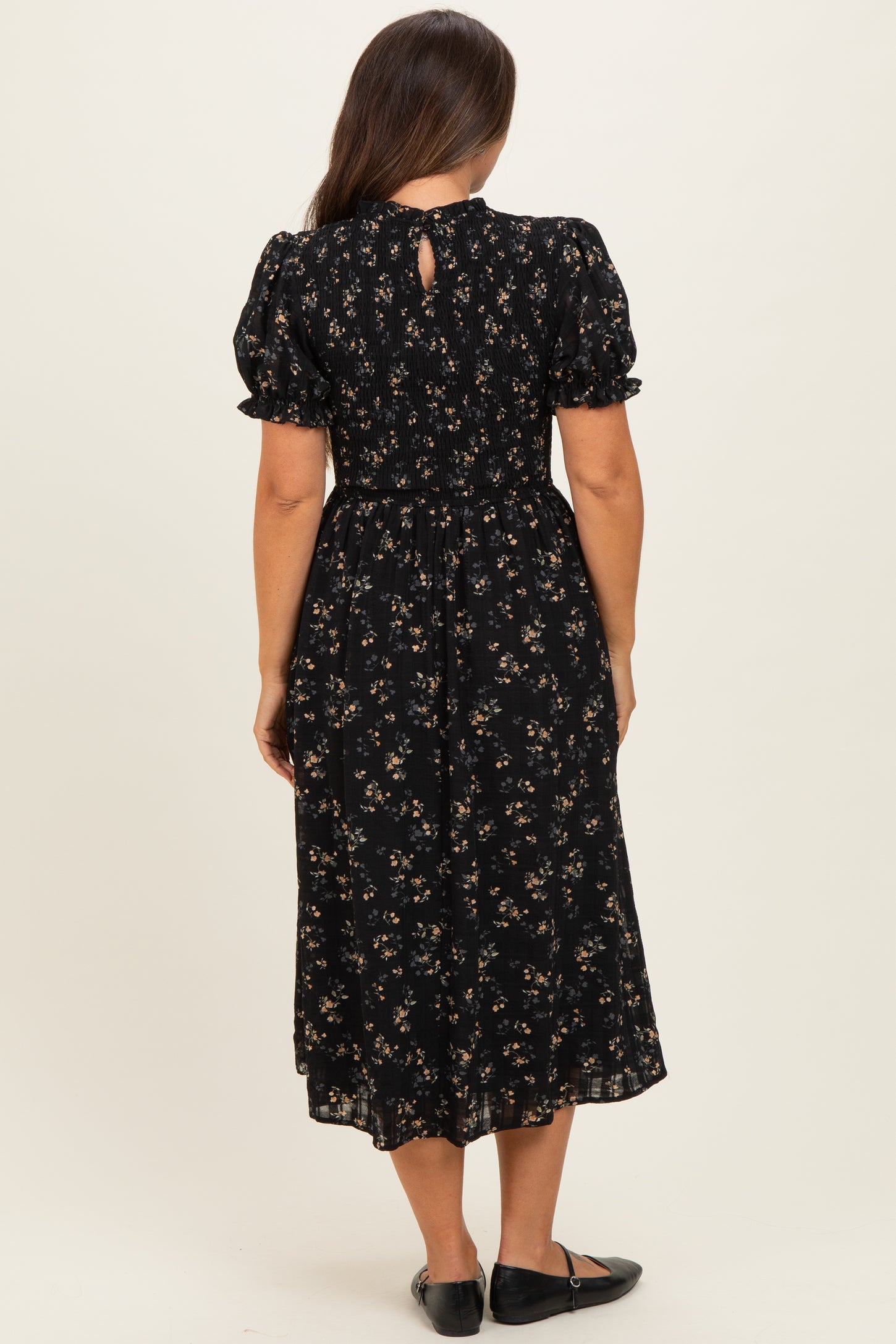 woman wearing a black floral maternity dress with short puff sleeves and a smocked bodice, showing a keyhole back