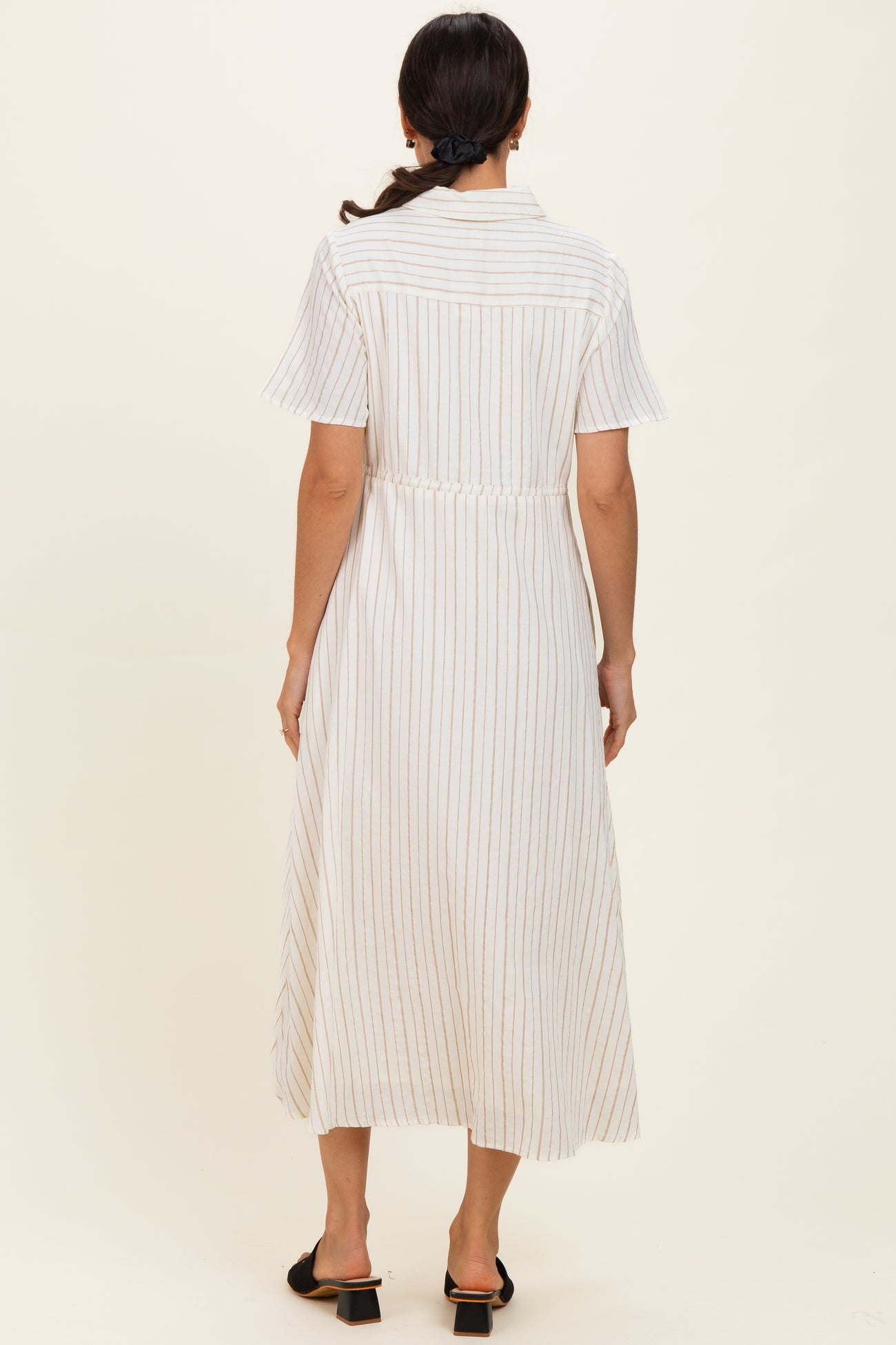 woman wearing a long white striped dress with short sleeves and a cinched waist, seen from the back