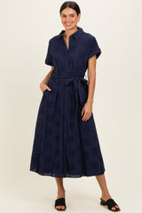 woman wearing a navy blue button-up midi dress with short sleeves, a tie waist, and floral eyelet details