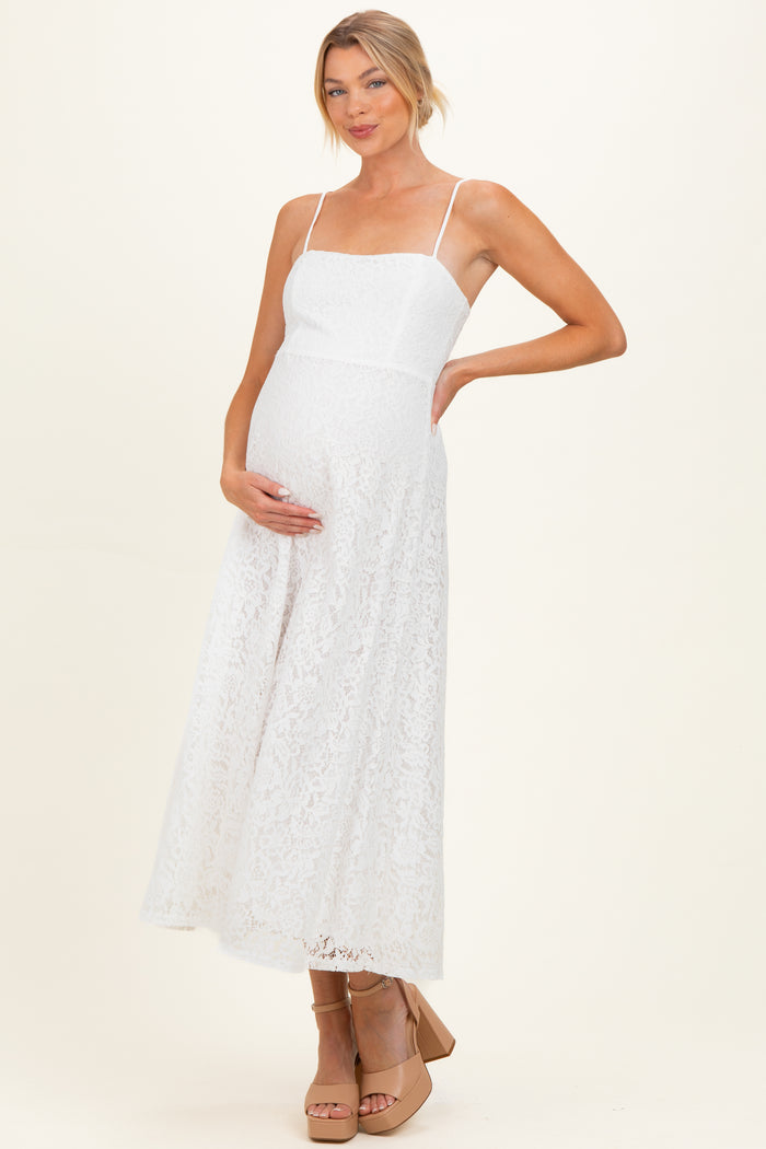 woman wearing a white lace maternity dress with spaghetti straps and holding her baby bump