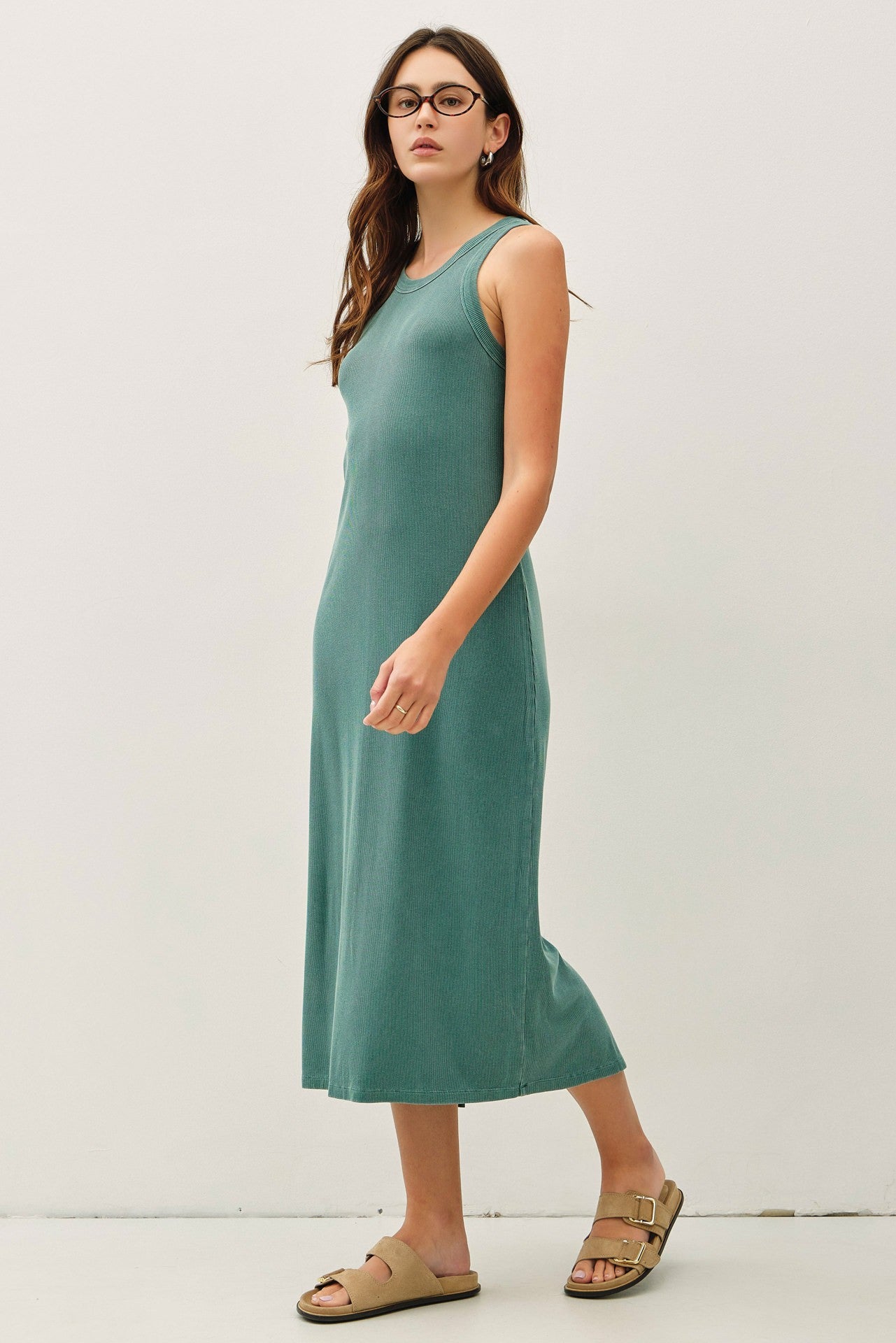 woman wearing a teal ribbed midi dress with a scoop neckline and sandals, standing against a plain background