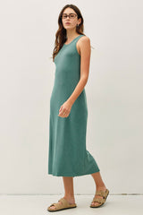 woman wearing a teal ribbed midi dress with a scoop neckline and sandals, standing against a plain background