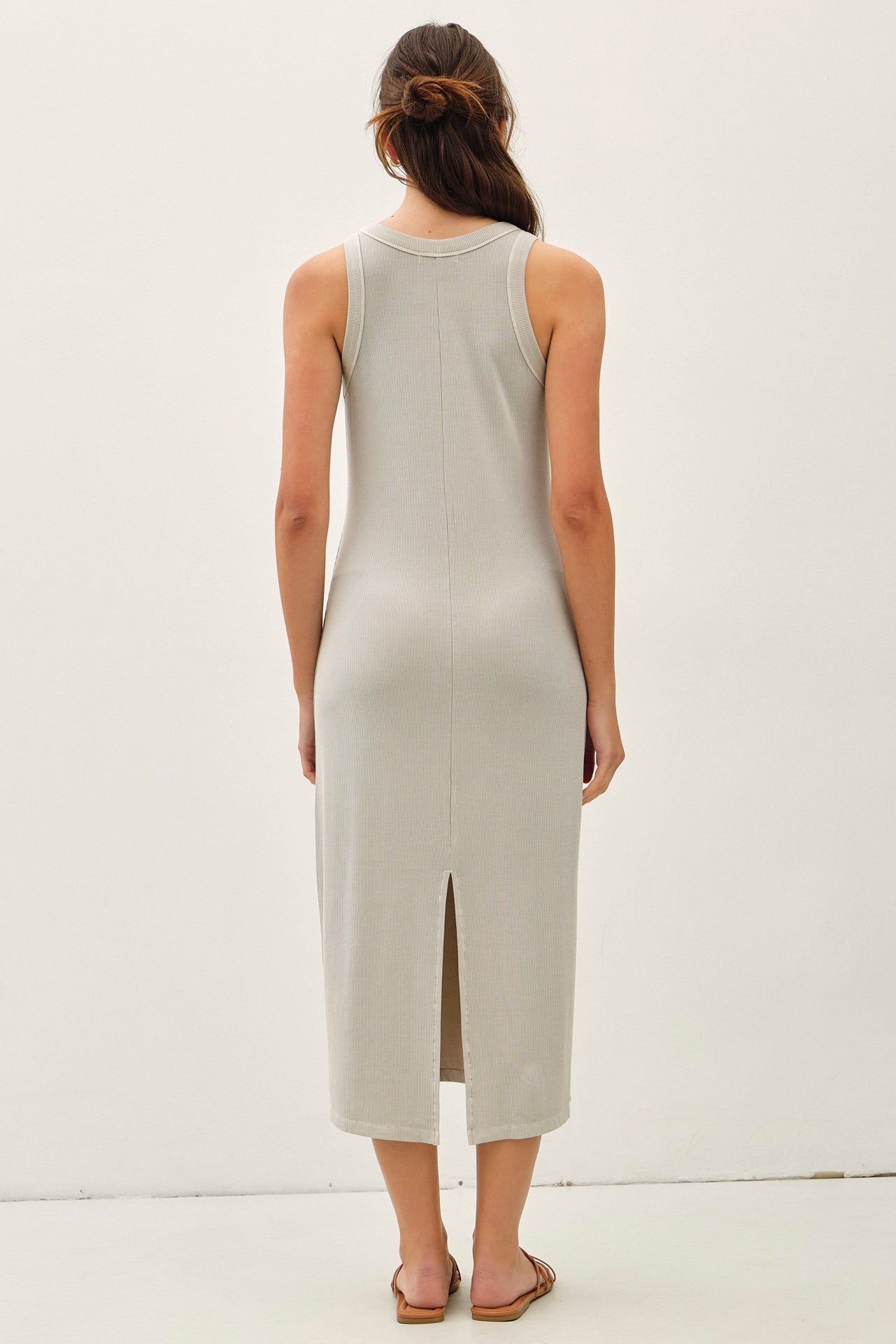 woman wearing a light gray sleeveless maxi dress with a back slit and open back
